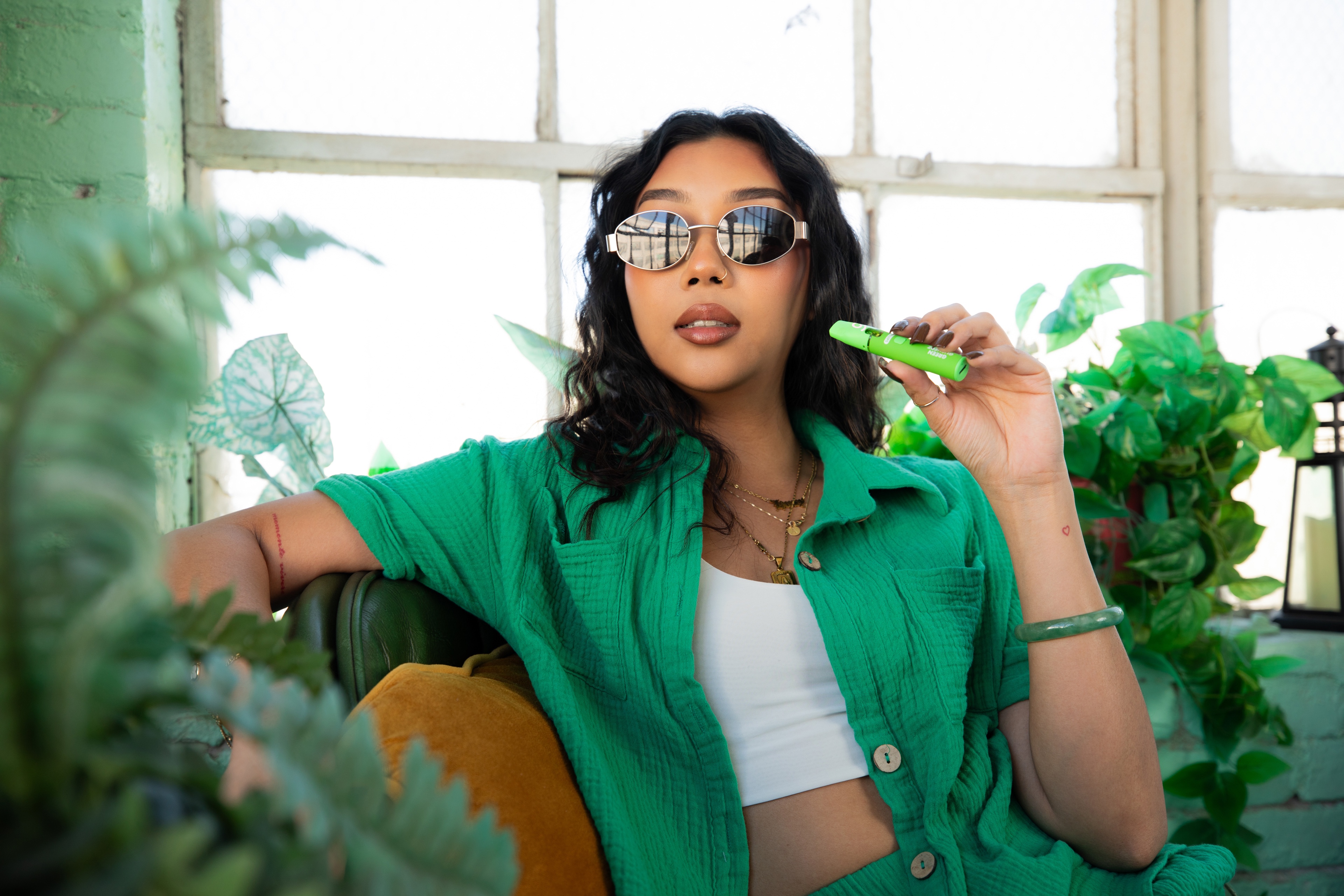 Woman in green holding a Cure Injoy vape in a bright plant-filled room